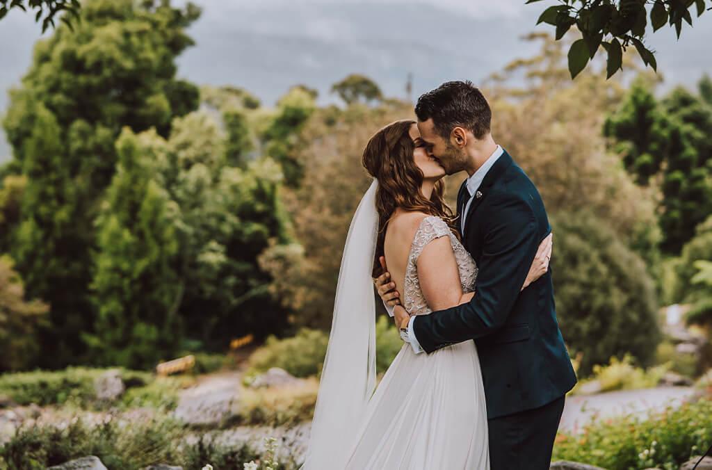 Bride and groom kiss in sunny garden with views of mountains. Credit: Avame Photography