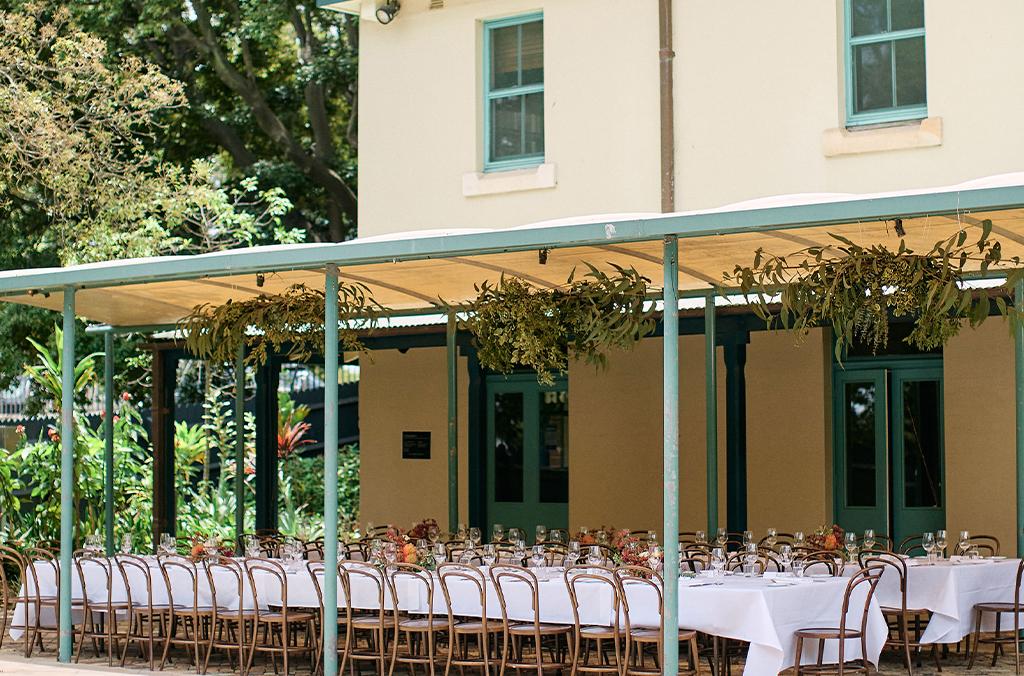 Shaded patio with long tables set with white tablecloths and dinnerware
