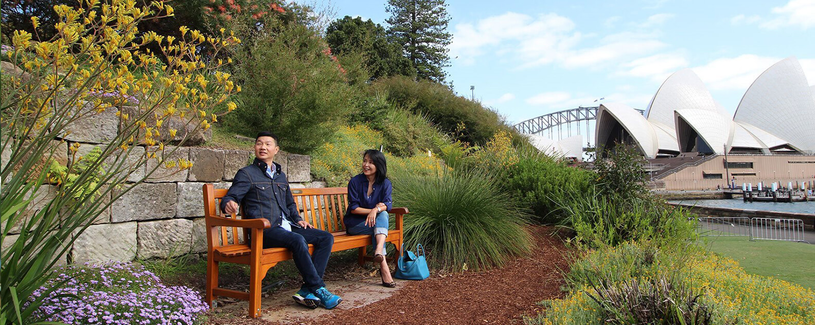 two people sit on a bench with sydney opera house in background