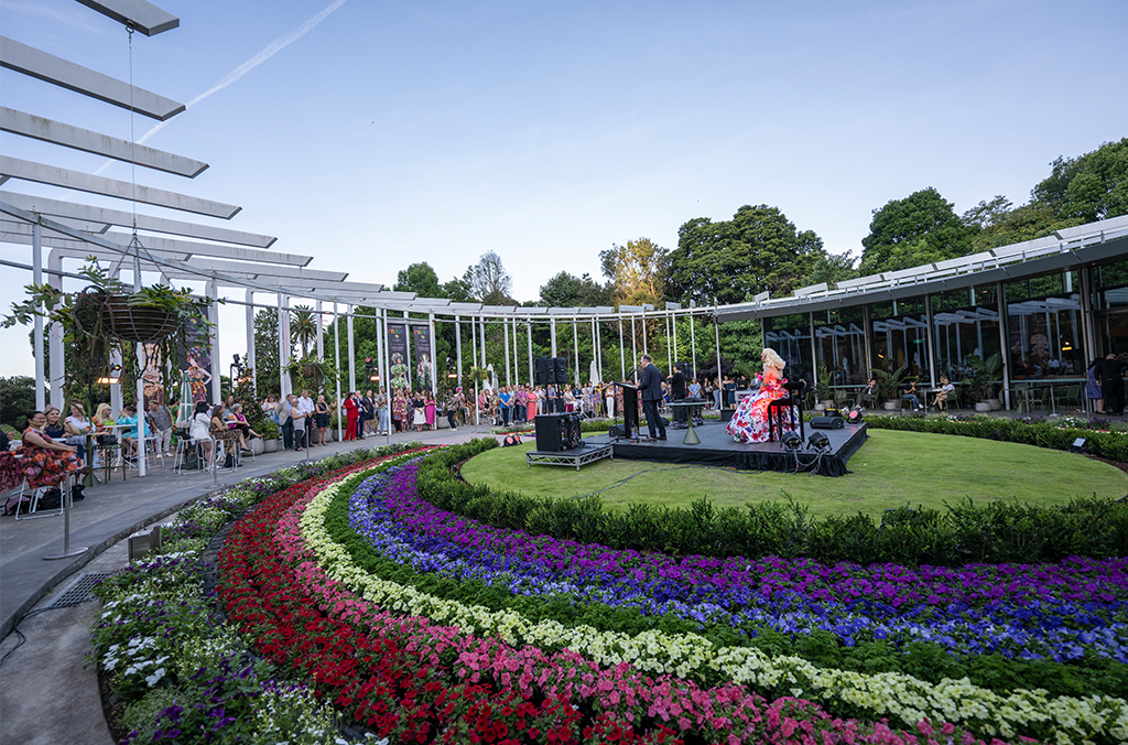 A crowd of people in the outdoor area, with rainbow flower displays