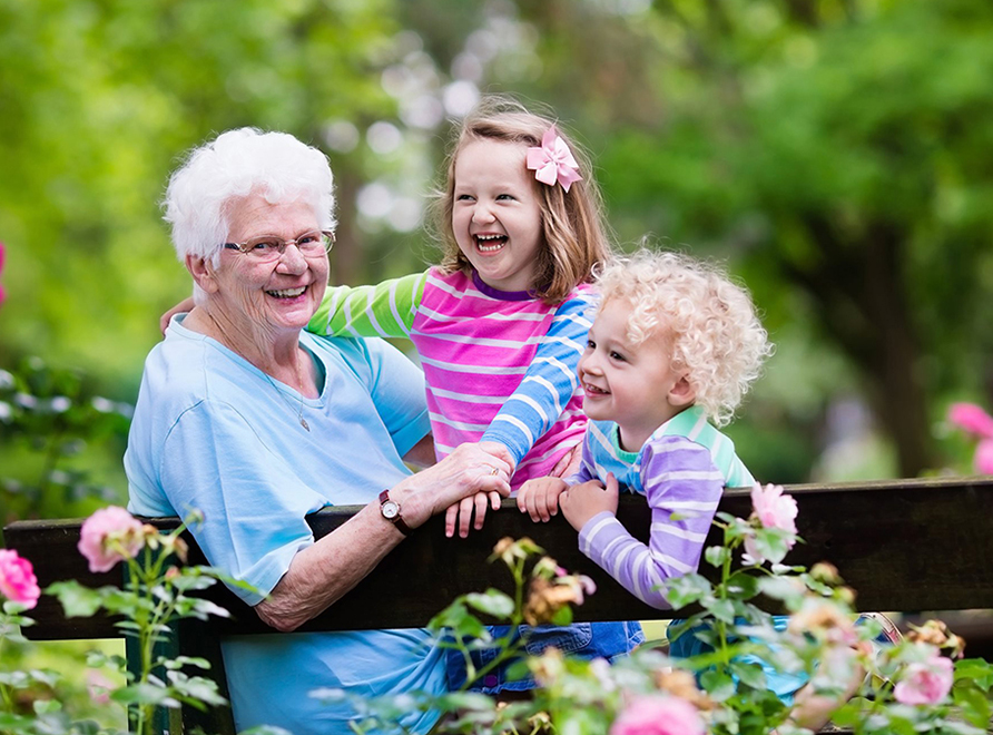 elderly lady sitting with two children next to rose garden