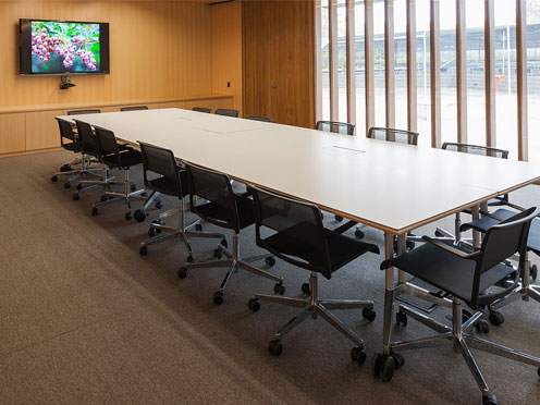 Corporate meeting room with wood panelling, wall to ceiling windows, a large meeting table with seating and a presentation screen.