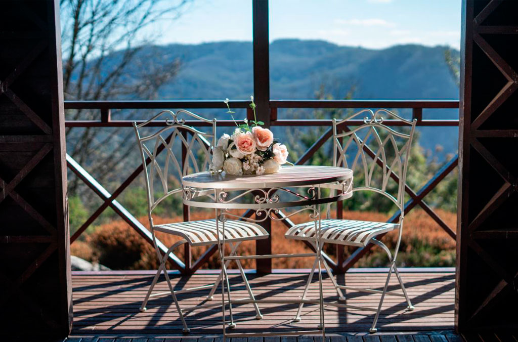 Romantic scene of wire chairs and table with wedding bouquet on the deck of the Northern Pavilion with the Blue Mountains in the background.