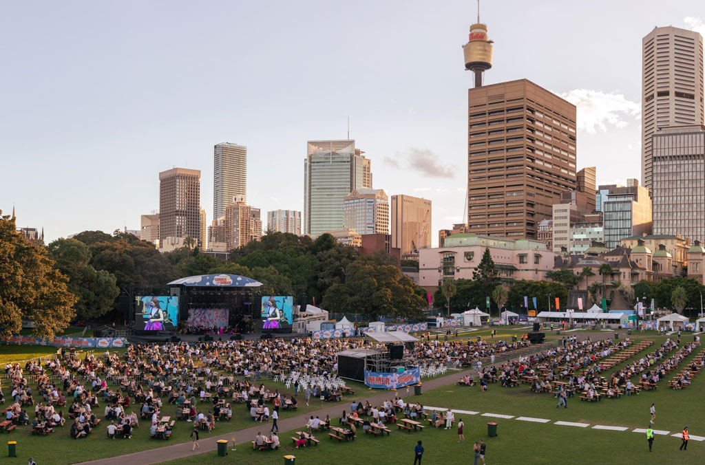 A socially-distanced, seated crowd in the Domain watching a concert with Sydney city skyline in the background