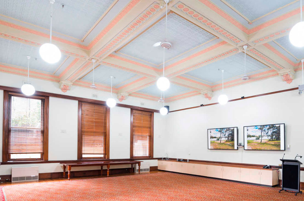 Renovated Victorian-era room with carpet, painted ceiling mouldings, wooden window frames and blinds.