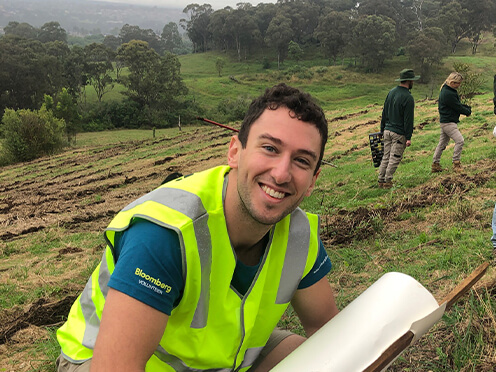 Volunteer in yellow high vis vest planting a sapling