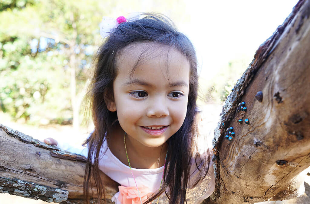 Girl poking head through tree during Nature Play