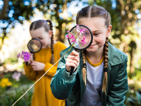 An outdoor scene, two students with magnifying glasses looking at orchids