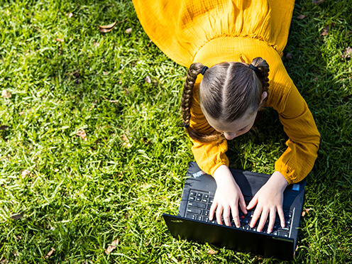 Child lying on lawn with a laptop