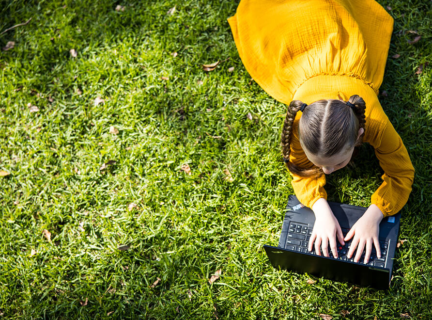 Child lying on lawn with a laptop