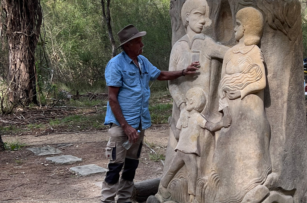 First Nations man puts his hand to the sculpture of a family together