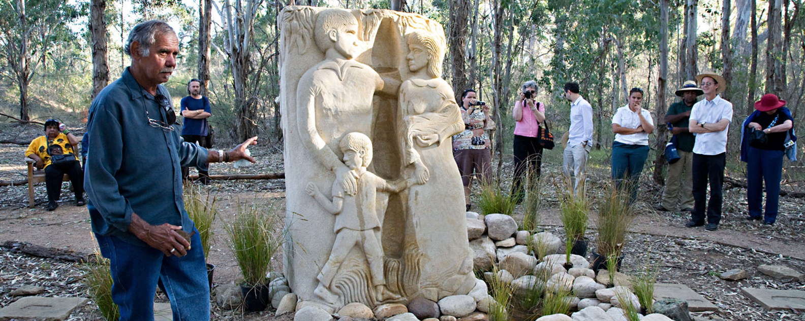 Stone sculpture of a mother, father and child, with people standing around it
