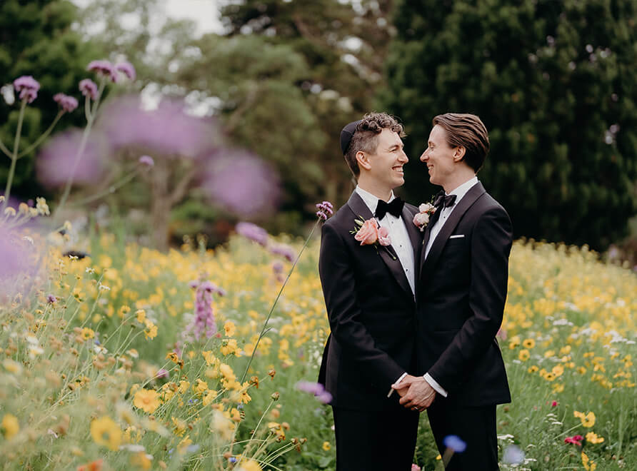 Michael and Jacob in wedding finery, holding hands in the wildflower meadow. Image: Russell Stafford Photography