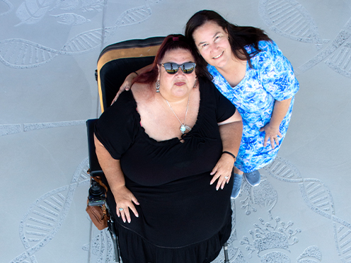 Two women on a concrete patio which is sandblasted into an elaborate First Nations artwork.