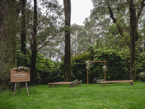 Lawn surrounded by tall eucalyptus trees, with rustic benches, flower arbour and a welcome sign ready for a wedding