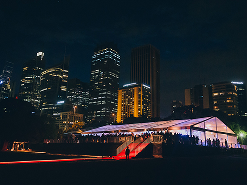 Marquee set up for an event on a lawn at night, with city skyline behind it