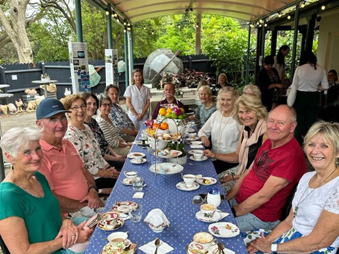 Long table with morning tea spread and smiling people sitting around
