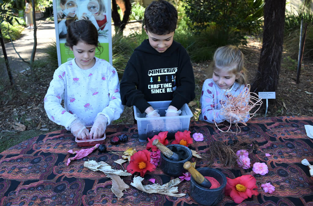 Three children with flowers, fruits and bowls of coloured powder dyes