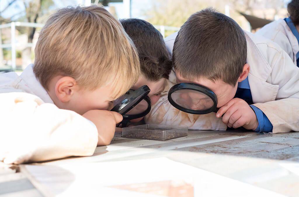 Three kids using magnifying glasses