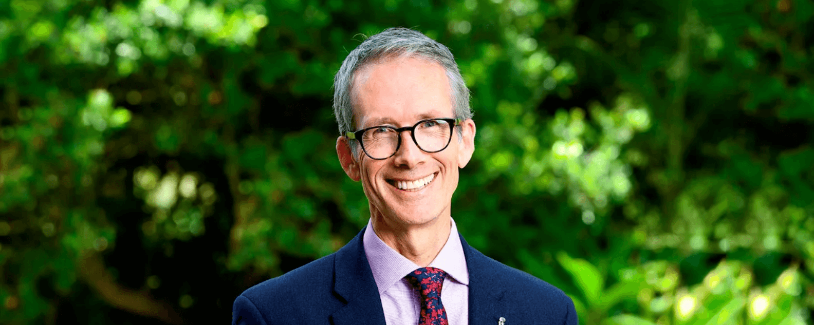 Tim Entwisle smiling at the camera with green trees and plants in the background
