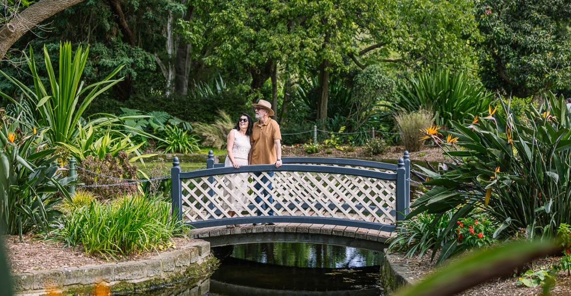 two people on bridge over creek, surrounded by tropical garden