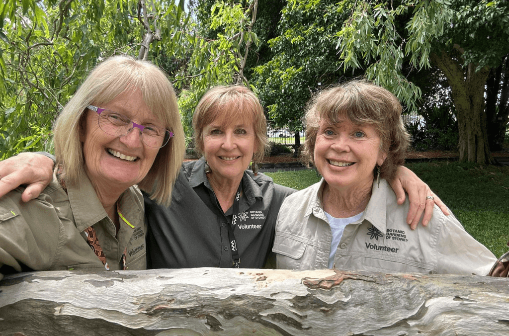 3 volunteer guides in front of a gum tree trunk smiling