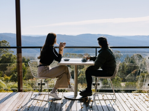 two people have coffee on a deck overlooking Blue Mountains views.