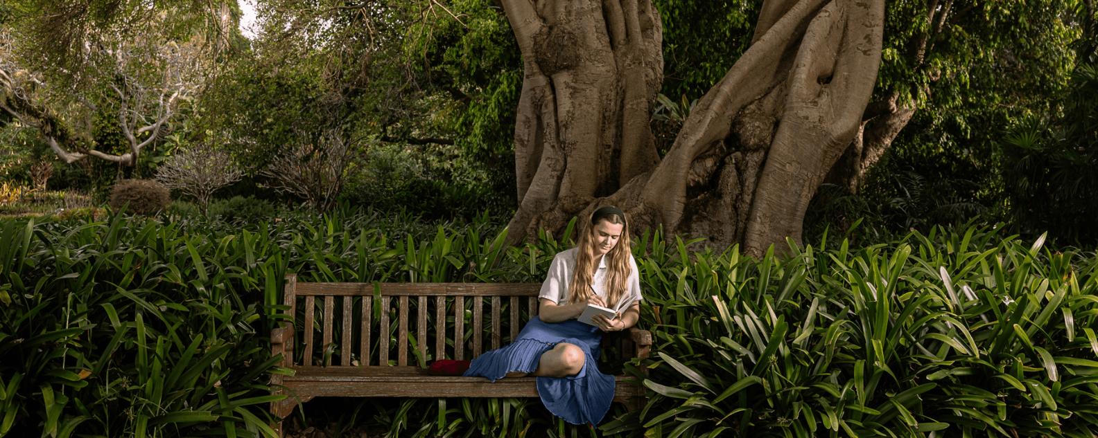 a woman sitting and writing on a bench