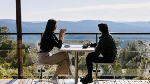 two people have coffee on a deck overlooking Blue Mountains views.