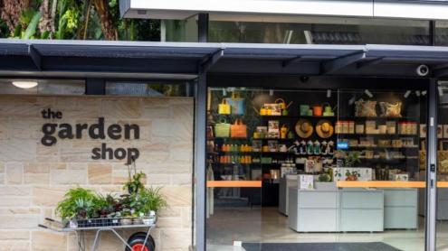 Outside of Garden shop, with a wheelbarrow of plants at the entrance and shelves of homewares, books and gifts seen through the windows.