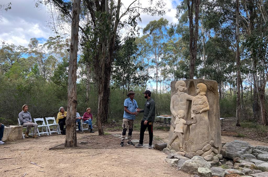 Members of the First Nations local community gather around a sculpture of a family