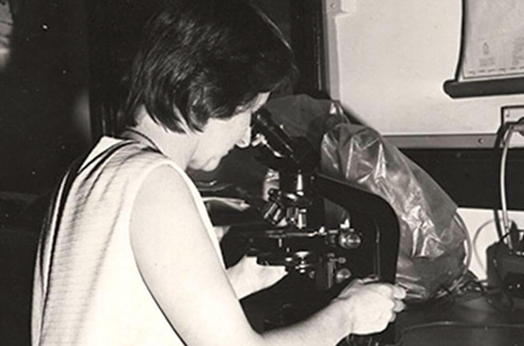 Black and white photo of one of the Gardens' longest serving scientists, Barbara Briggs looking at a specimen with a microscope.
