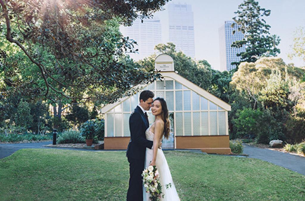Bride and groom cuddle in front of historic, shabby chic green house wedding venue