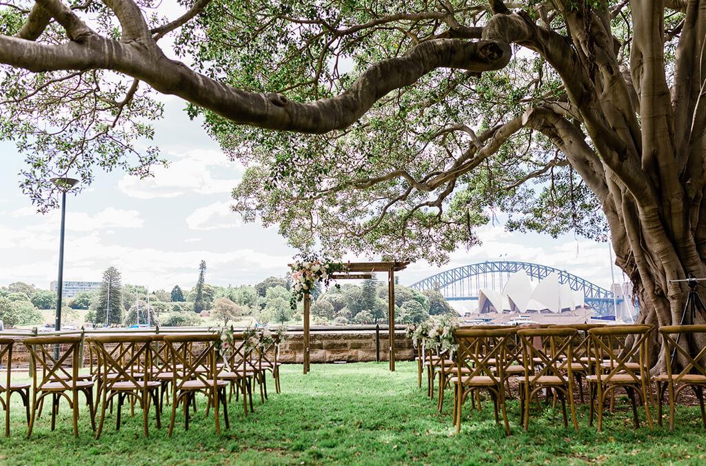 Chairs and wedding ceremony arch set up, under fig tree and overlooking Sydney Harbour