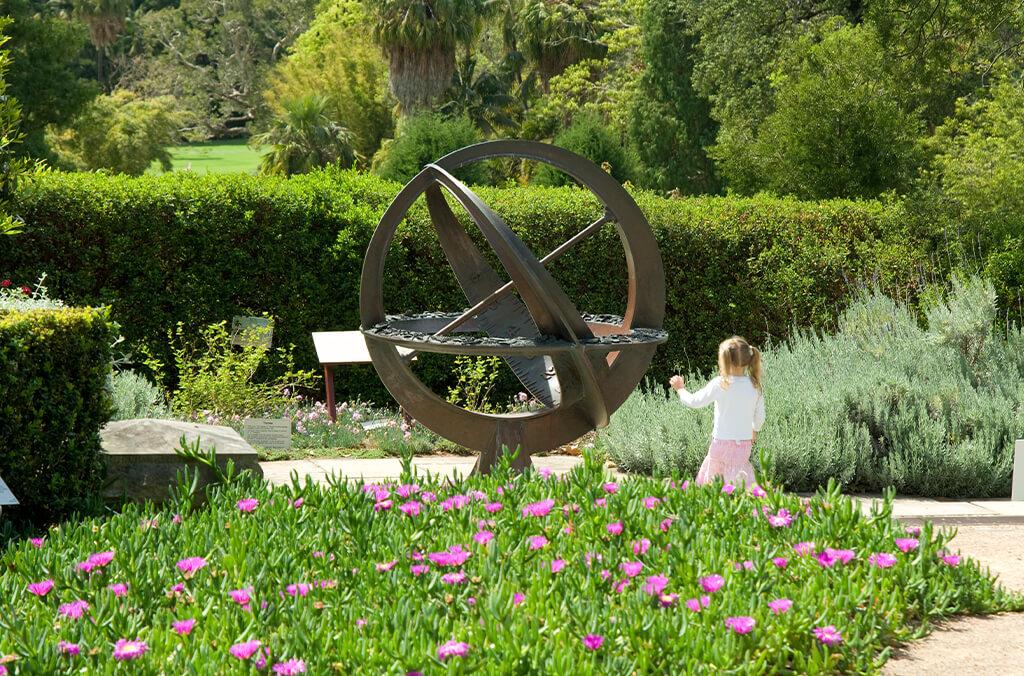 Compass sculpture in a lush green Garden, child running past