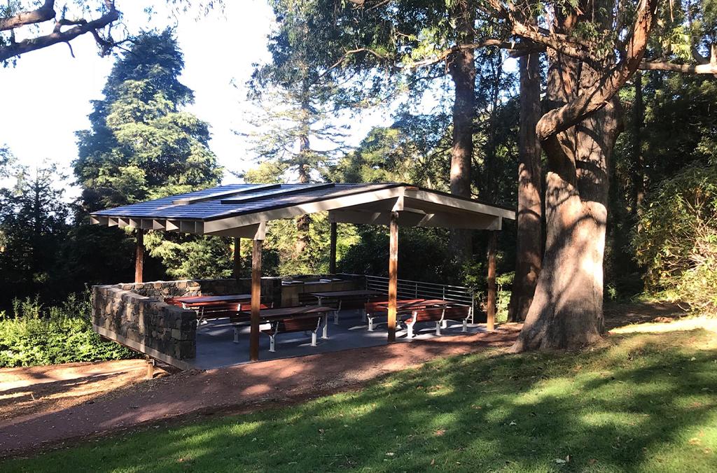 Picnic shelter in shady garden, with picnic tables and barbeques