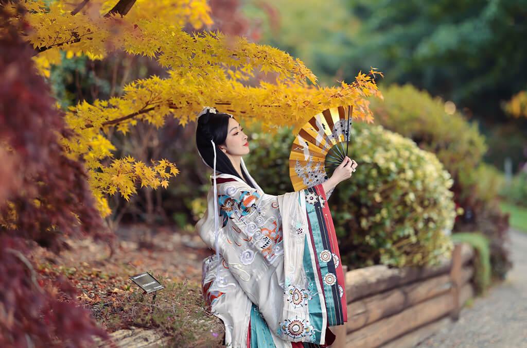 Woman in traditional Chinese Han attire, rests among spectacular golden maples