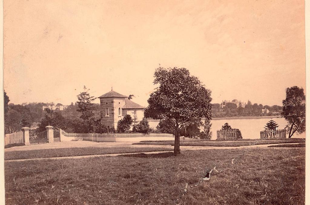 Old black and white photo of sandstone cottage with fields and Sydney Harbour surrounding it