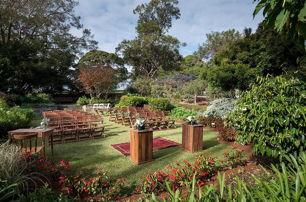 Lawn surrounded by lush garden, with chairs set up for a wedding ceremony