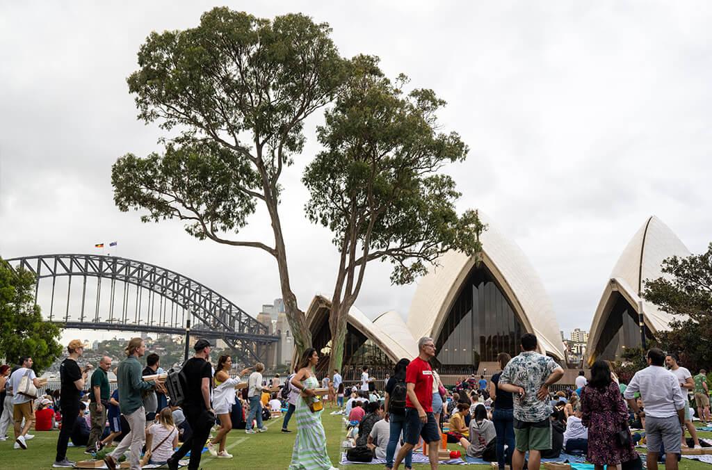 People setting up picnics on lawn overlooking Sydney Opera House and Harbour Bridge