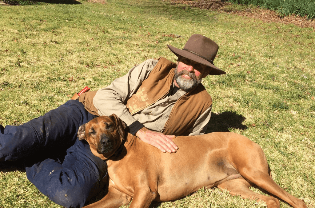 Rick Sheperd lying on the grass with his brown dog
