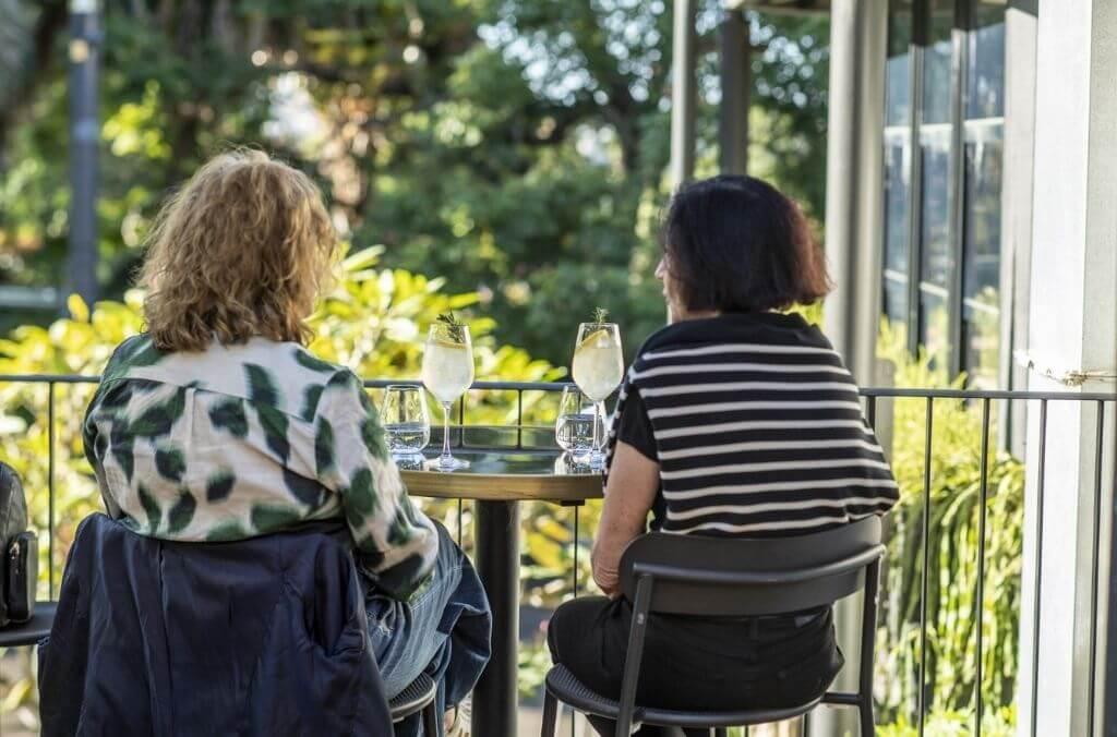 Two women with cool drinks at a restaurant overlooking gardens