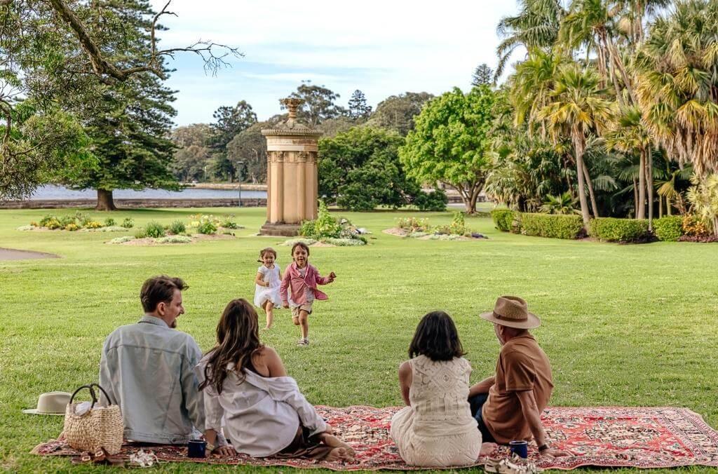 Family picknicking on lawn, and children running around playing.