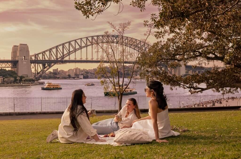 Three friends chilling out on lawn overlooking Sydney Harbour