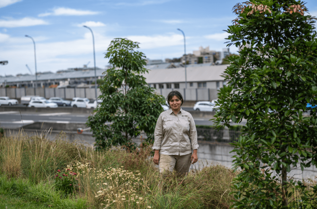 A woman stands in a meadow field against a highway